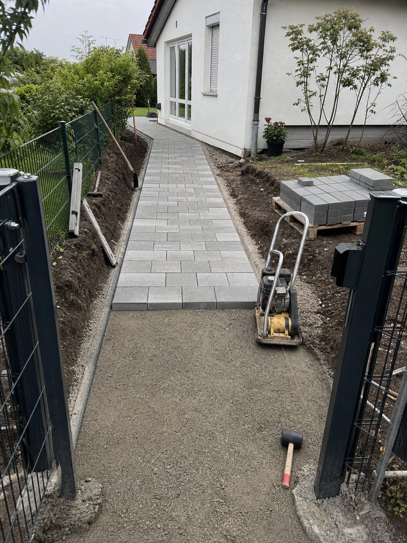 Gartenweg im Bau mit Verdichtungsgerät und Pflastersteinen